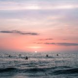 anonymous travelers swimming in wavy sea at sundown